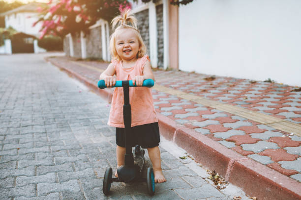Child girl riding scooter on city street happy baby 1 year old healthy active lifestyle family fun outdoor stock photo