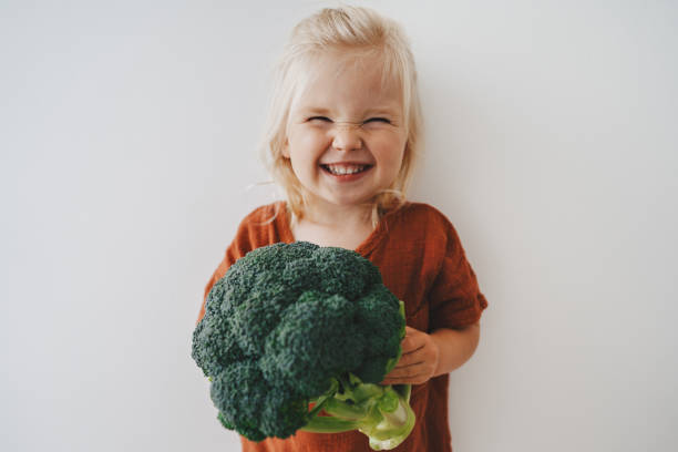 Child girl with broccoli healthy food vegan eating lifestyle organic vegetables plant based diet nutrition funny kid happy smiling stock photo
