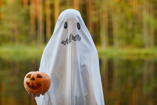 Child in Ghost Costume on Halloween Waist up portrait of spooky child dressed as ghost holding pumpkin standing outdoors on Halloween, copy space ghost boy stock pictures, royalty-free photos & images