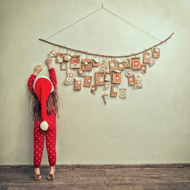 child in pajamas and Christmas cap stretches for advent calendar with small gifts. kid counts days until new year child in pajamas and Christmas cap stretches for advent calendar with small gifts. kid counts days until new year. advent stock pictures, royalty-free photos & images