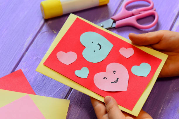 Child is holding a Valentines card in his hands. Child is showing a greeting card. Happy Valentines Day card. Easy paper crafts for kids concept. Closeup stock photo