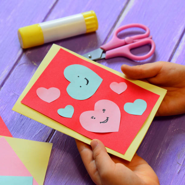 Child is holding a Valentines day greeting card in his hands. Small child is showing a Valentines day greeting card gift surprise. Cute and easy paper art for kindergarten. Paper cut out hearts. Closeup. Paper crafts for home. Easy paper crafts for kids stock photo