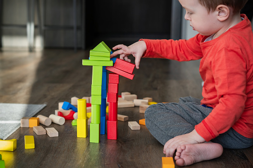 Child, little boy, toddler playing with eco-friendly wooden bricks or blocks at home. Children's game space at home. Creative indoors activities for kids.