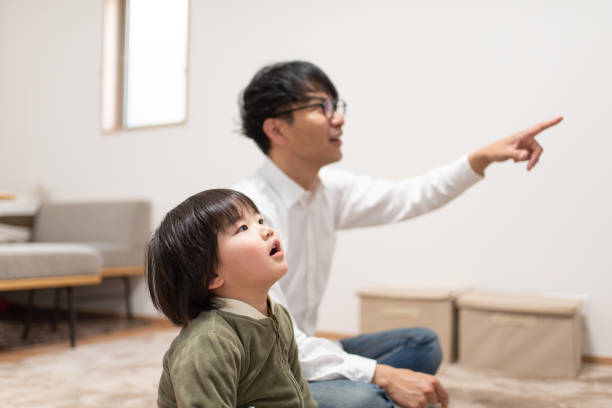 Child looking at TV with father in room Child looking at TV with father in room asian kids watching tv stock pictures, royalty-free photos & images