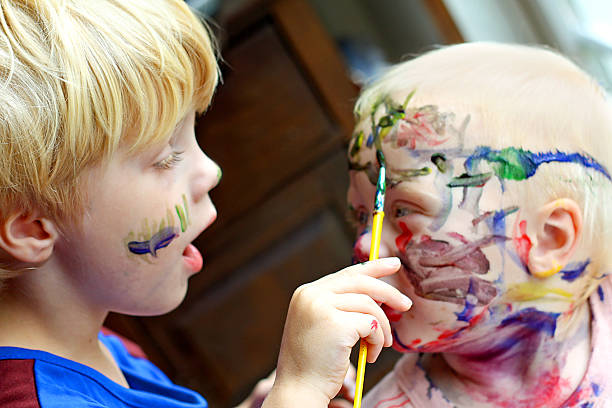 Child Painting his Baby Brother's Face a Small child is painting the face of his baby brother, with colorful rainbow colors child behaving badly stock pictures, royalty-free photos & images
