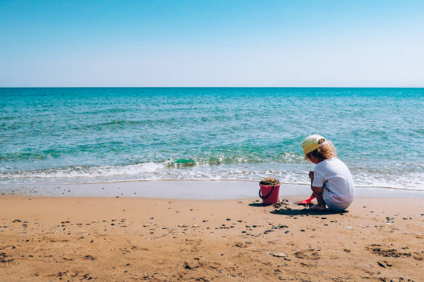 A child plays with a pink plastic bucket and shovel in the sand on a beach A child plays with a pink plastic bucket and shovel in the sand on a beach, close to the sea. Crete, Greece. human feet buried in sand. summer beach stock pictures, royalty-free photos & images