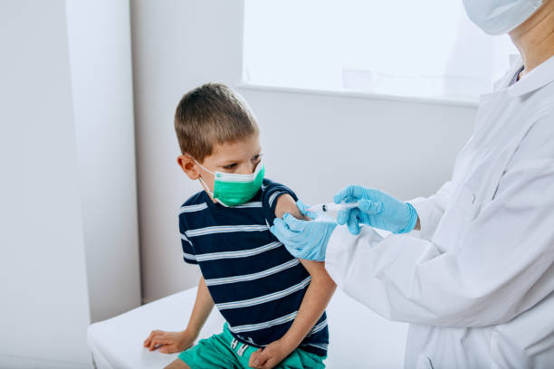 Child Receiving Vaccination Shot From Doctor A  Caucasian boy receives a vaccine, possibly for COVID-19 Coronavirus, administered by a female Dr. vaccine mandate stock pictures, royalty-free photos & images