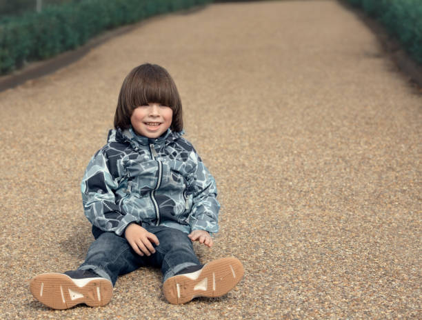 Child smiles and sits on the ground stock photo