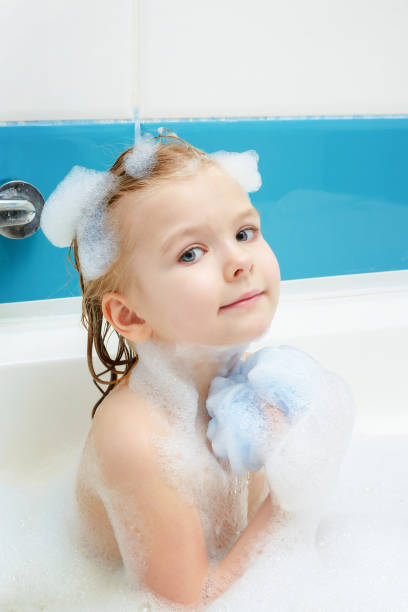 Child soaping washcloth for the body. Little girl is taking a bubble bath. Light photo. stock photo