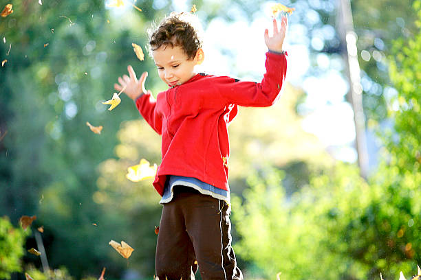 Child tossing autumn leaves into the air stock photo