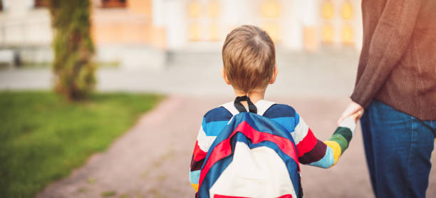 Child with rucksack and with mother in front of a school building stock photo