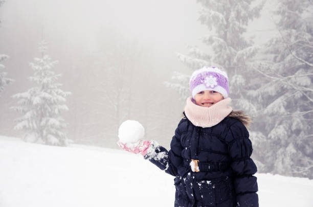 child with snowball in winter forest stock photo