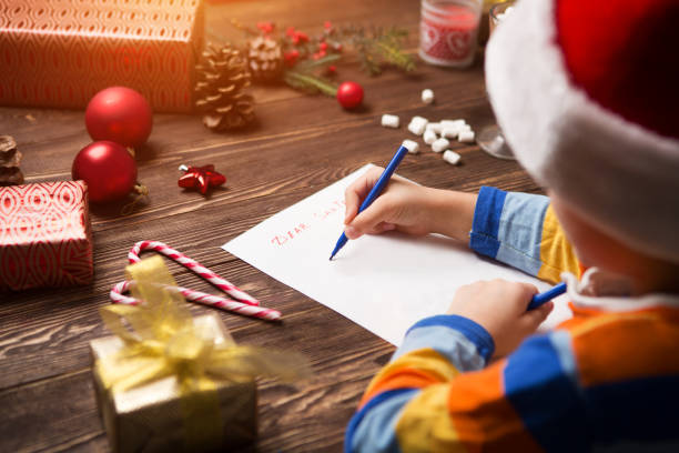 child writes the letter to santa claus on wooden background with decorations. - a letter to santa claus, christmas gifts imagens e fotografias de stock