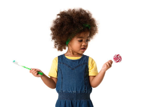 childhood and people concept- lovely african american little girl with toothbrush and sweet lolipop. Healthy teeth concept. Unhealthy food. childhood and people concept-lovely african american little girl with toothbrush and sweet lolipop. Healthy teeth concept. Unhealthy food. rotten teeth in children stock pictures, royalty-free photos & images