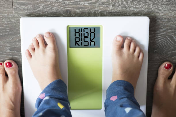 Childhood obesity high risk for health problems with child’s feet on weight scale  under the supervision of his mother stock photo