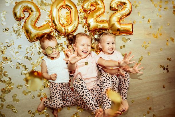 Children, 3 sisters, celebrating the new year 2022 at home, laughing in confetti stock photo