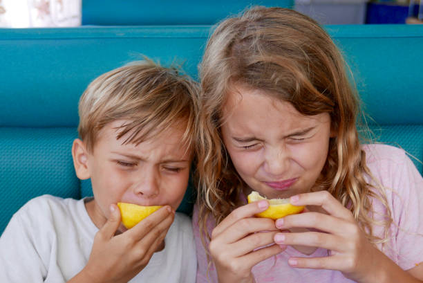 Children biting into lemons and making faces stock photo