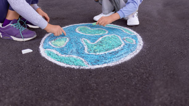 Children boy and girl draw a planet globe with a world map drawn with chalk on the asphalt. Side view.​​​ foto