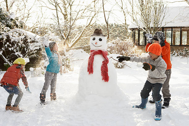 Children building a snow man and having a snowball fight stock photo