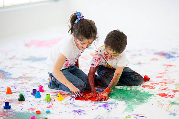 Children Doing Art Therapy A brother and sister are creatively playing with finger paints for art therapy. The children and the white background is covered with hand prints, paint splatters, and colorful paint. art therapy stock pictures, royalty-free photos & images