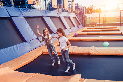 Little pretty girls having fun outdoor. Jumping on trampoline in children zone. 