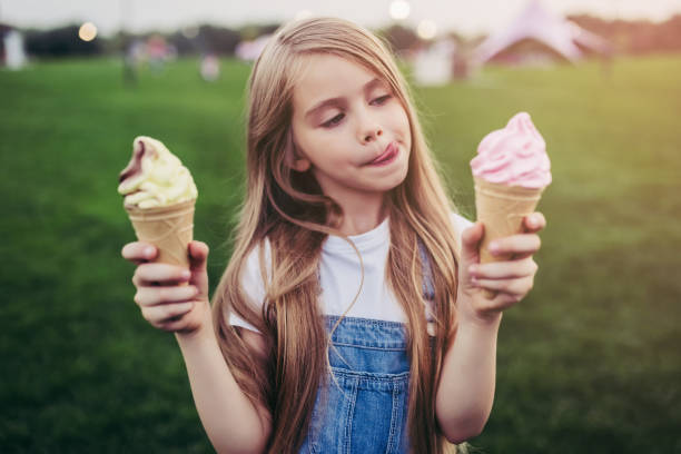Children having fun. Little pretty girl is having fun outdoor. Standing on green grass and with ice cream in hands. cream dairy product stock pictures, royalty-free photos & images
