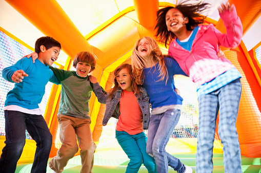 Multi-ethnic group of excited children (ages 7 to 10 years) jumping in inflatable bouncy castle.