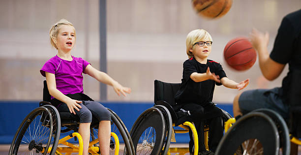 An action shot with motion blur of disabled children playing with basketballs in an indoor gym.