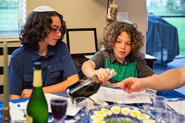 Brothers are sitting at a dinning room table participating in a Passover seder.  rm