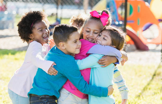 Children playing outdoors on playground, hugging A multi-ethnic group of children playing outdoors on a playground on a sunny day. They are all playfully hugging each other. recess stock pictures, royalty-free photos & images