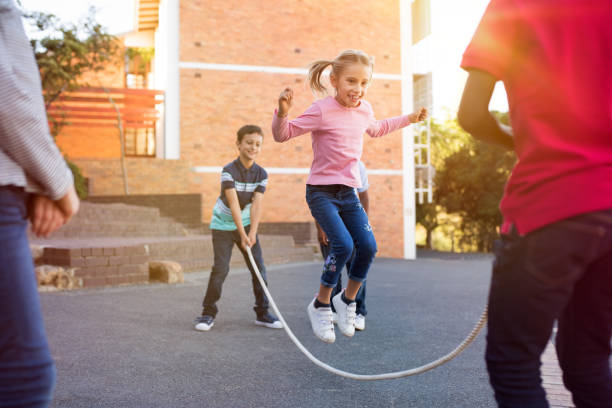 Children playing with skipping rope Happy elementary kids playing together with jumping rope outdoor. Children playing skipping rope jumping game and laughing outdoors. Happy cute girl jumping over skipping rope held by her friends. courtyard stock pictures, royalty-free photos & images
