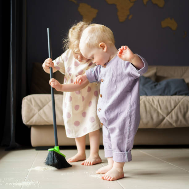 Children sister and brother sweeping floor with broom at home stock photo