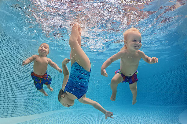 children swim and dive underwater with fun in swimming pool - swimming baby stockfoto's en -beelden