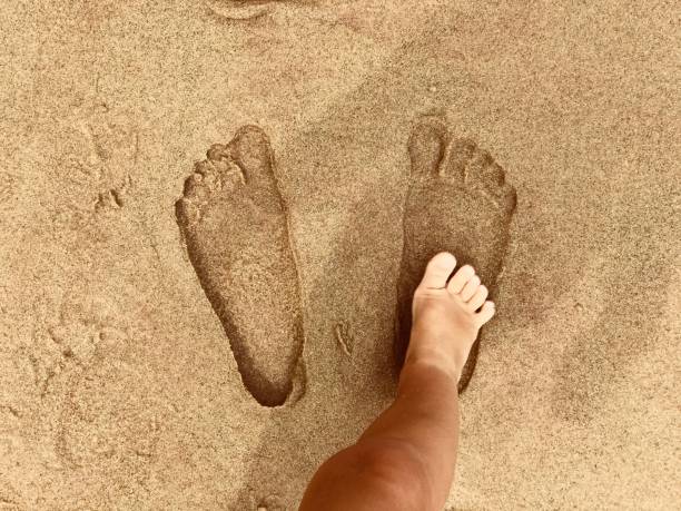 Children toddler foot stepping on large footsteps on the sand stock photo