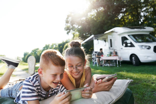 kinderen die mobiele telefoons gebruiken terwijl het op het kamperen zijn - camping stockfoto's en -beelden