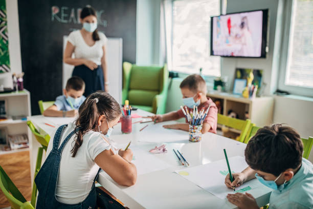 Children with protective face masks drawing in preschool Preschool childern with protective face masks drawing in preschool. Firts day at school after reopening during coronavirus pandemic. child care stock pictures, royalty-free photos & images