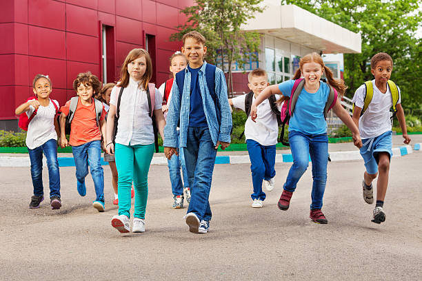 children with rucksacks near school walking - hogeschool rood samen stockfoto's en -beelden
