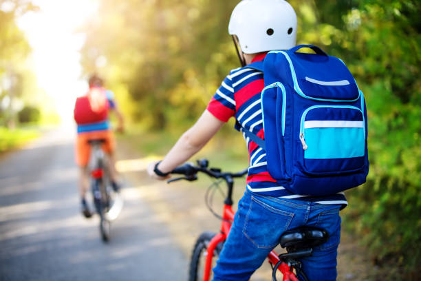 Children with rucksacks riding on bikes in the park near school. stock photo