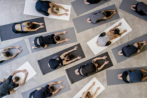 Child's Pose An aerial shot of a multi ethnic group of men and women practice yoga on on mats while wearing grey, black and white in an industrial setting. They are reaching forward in child's pose. studio workplace stock pictures, royalty-free photos & images