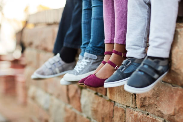 Chilling before class starts Cropped shot of unrecognizable  elementary school kids sitting on a brick wall outside shoe stock pictures, royalty-free photos & images