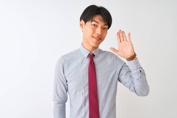 Chinese businessman wearing elegant tie standing over isolated white background Waiving saying hello happy and smiling, friendly welcome gesture  wave goodbye asian stock pictures, royalty-free photos & images