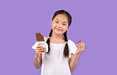 スタジオで紫色の背景の上にポーズチョコレートを食べる中国の女の子