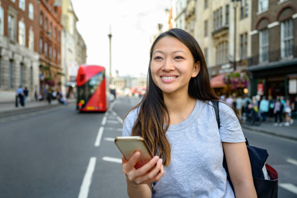 Chinese tourist in London checking smart phone for guidance Independent young Chinese woman using smart phone for sightseeing tips while vacationing in London. central london stock pictures, royalty-free photos & images