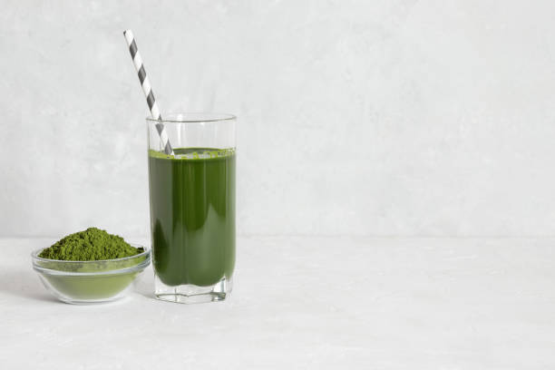 Chlorella green drink in a glass and powder in a bowl on a white concrete background. Detox drink and superfood concept. Natural supplement. Copy space. stock photo