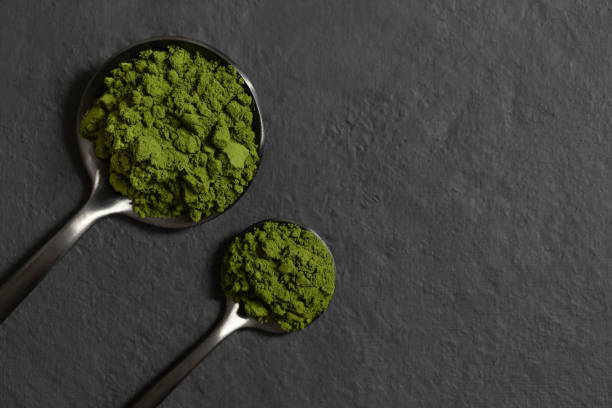 Chlorella or spirulina powder in spoons on a dark background. Green algae powder. Organic mineral supplement. Detox. View from above. Space for text. stock photo