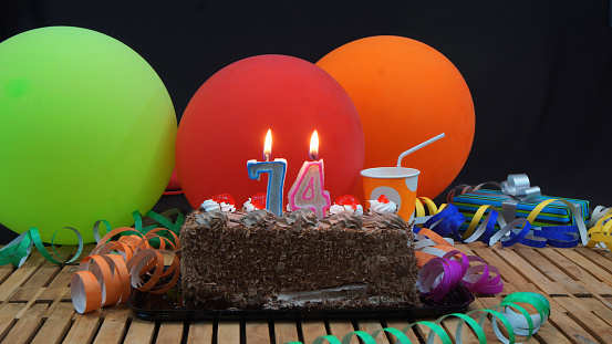 chocolate-74-birthday-cake-with-candles-burning-on-rustic-wooden-picture-id915537242