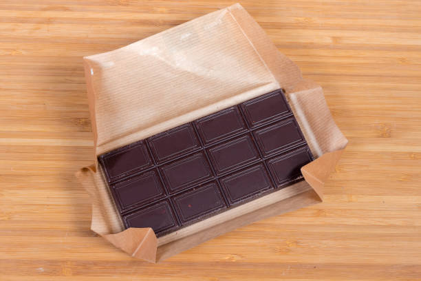 Chocolate bar in open paper wrapper on the wooden surface Bar of dark chocolate with nuts in open paper wrapper on the wooden surface, top view semi sweet chocolate stock pictures, royalty-free photos & images