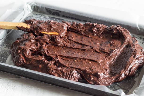 Chocolate brownie cake batter being placed in wax paper lined baking pan stock photo