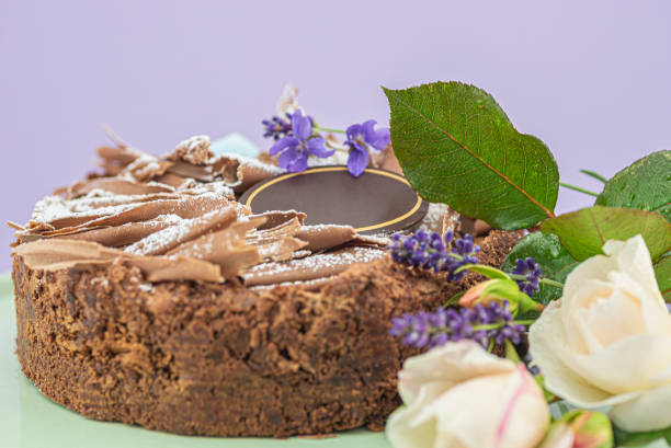 Chocolate cake with copy space and flowers A delicious chocolate cake decorated with chocolate shavings , powdered sugar, white roses, violets and lavender flowers. On top of the cake there is a blank sign made of chocolate and the sign is decorated with a golden stripe. The cake is on a turquoise cake stand. happy birthday in danish stock pictures, royalty-free photos & images