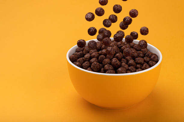 Chocolate Corn balls falling in bowl over yellow background Chocolate Corn balls falling in bowl over yellow background with copy space, healthy breakfast cereal breakfast cereal stock pictures, royalty-free photos & images